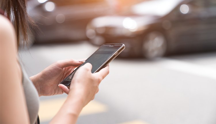 Frau mit Smartphone on der Hand auf der Straße: Uber Deutschland lockt mit Uber-Codes und Rabatten