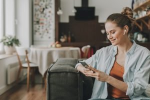 Eine Glückliche Frau sitzt mit Ihrem Smartphone auf dem Sofa und Lächelt